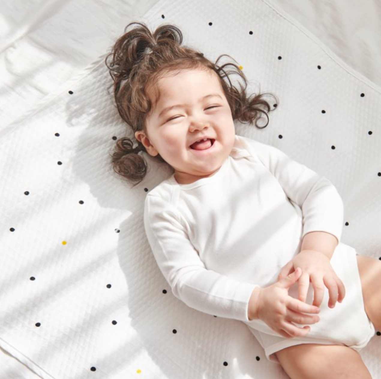 Smiling baby lying on a Little Dot waterproof mattress, made of cotton and polyester, perfect for diaper changing.