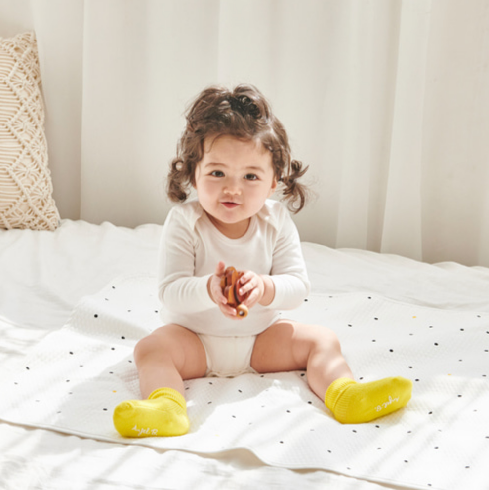 Baby sitting on Little Dot Waterproof Mat, wearing yellow socks, in a bright room