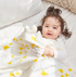 Baby wrapped in a bamboo rayon blanket with yellow star prints, lying in bed with a white pillow and woven cushion.