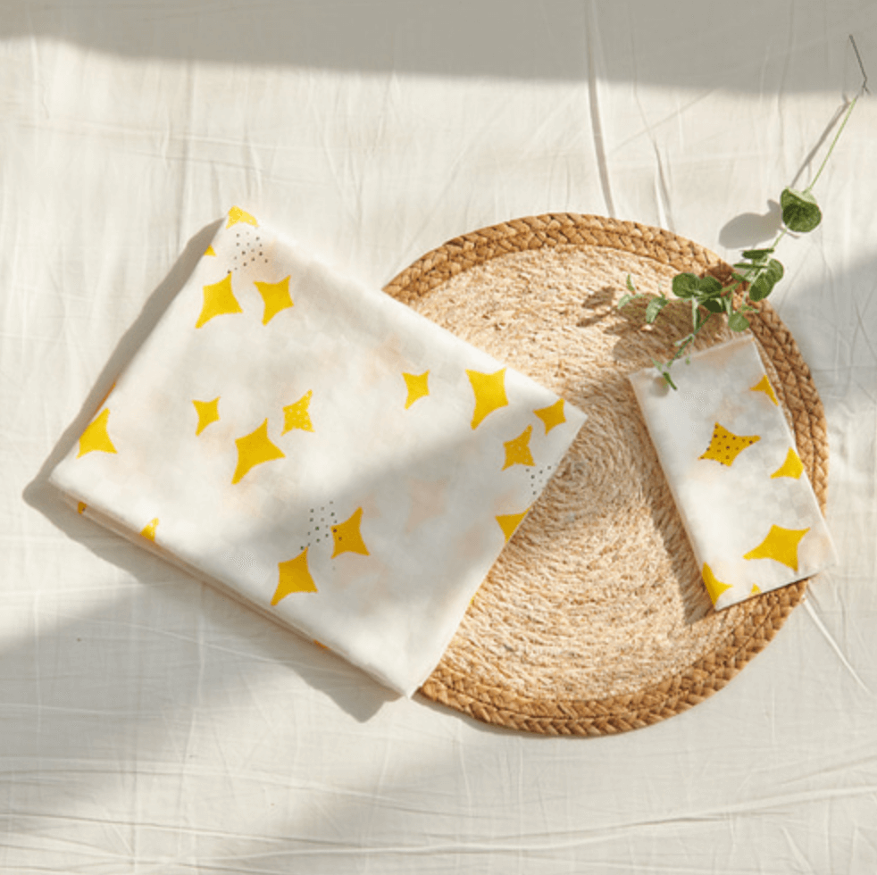 Bamboo blanket made of bamboo rayon, 100 x 90 cm, featuring yellow star patterns and made in Korea, displayed on a woven mat with greenery.