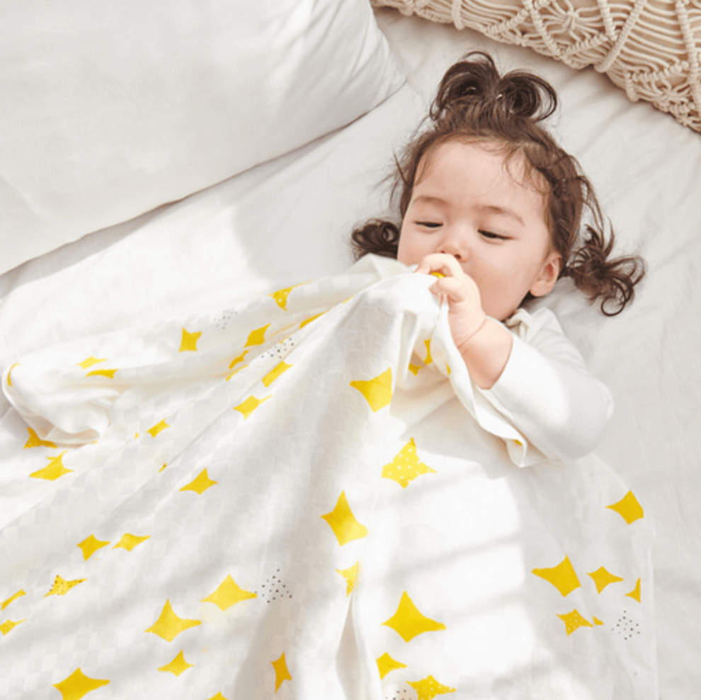 Toddler wrapped in soft bamboo blanket with yellow star patterns on a cozy bed.