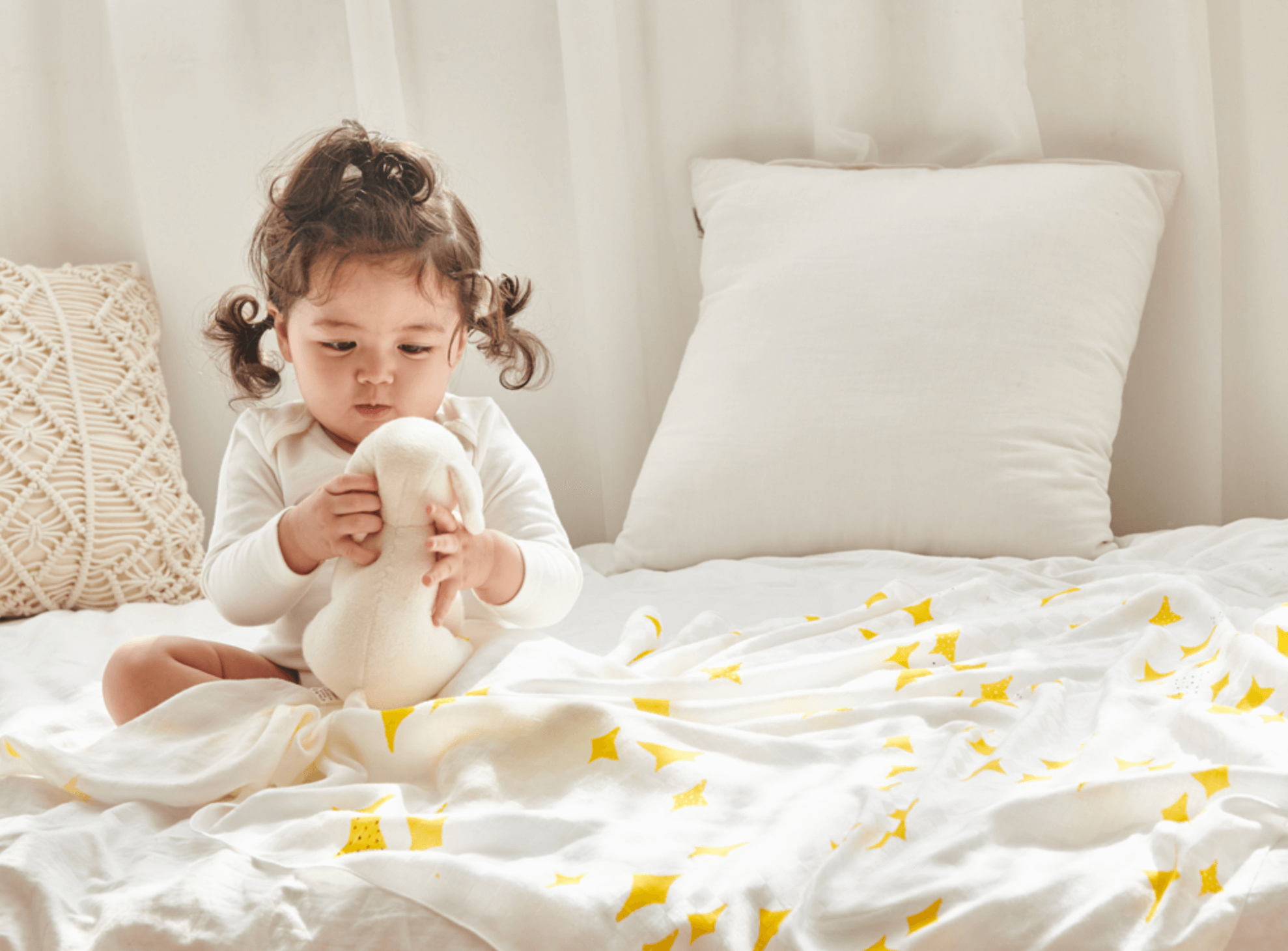 Toddler holding a stuffed toy on a bed with a soft bamboo blanket decorated with yellow stars